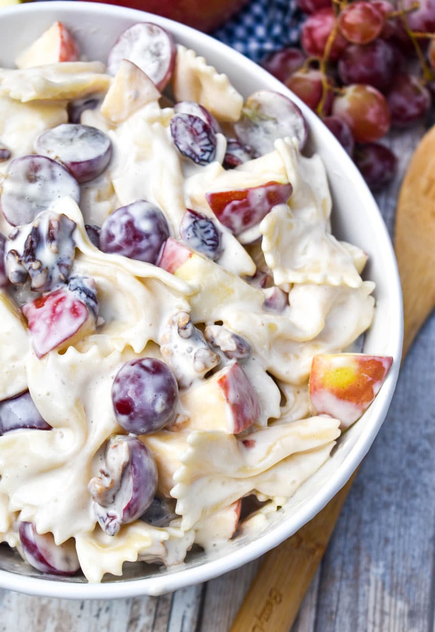 sweet pasta salad with fruit and honey in a white bowl surrounded by fresh fruits