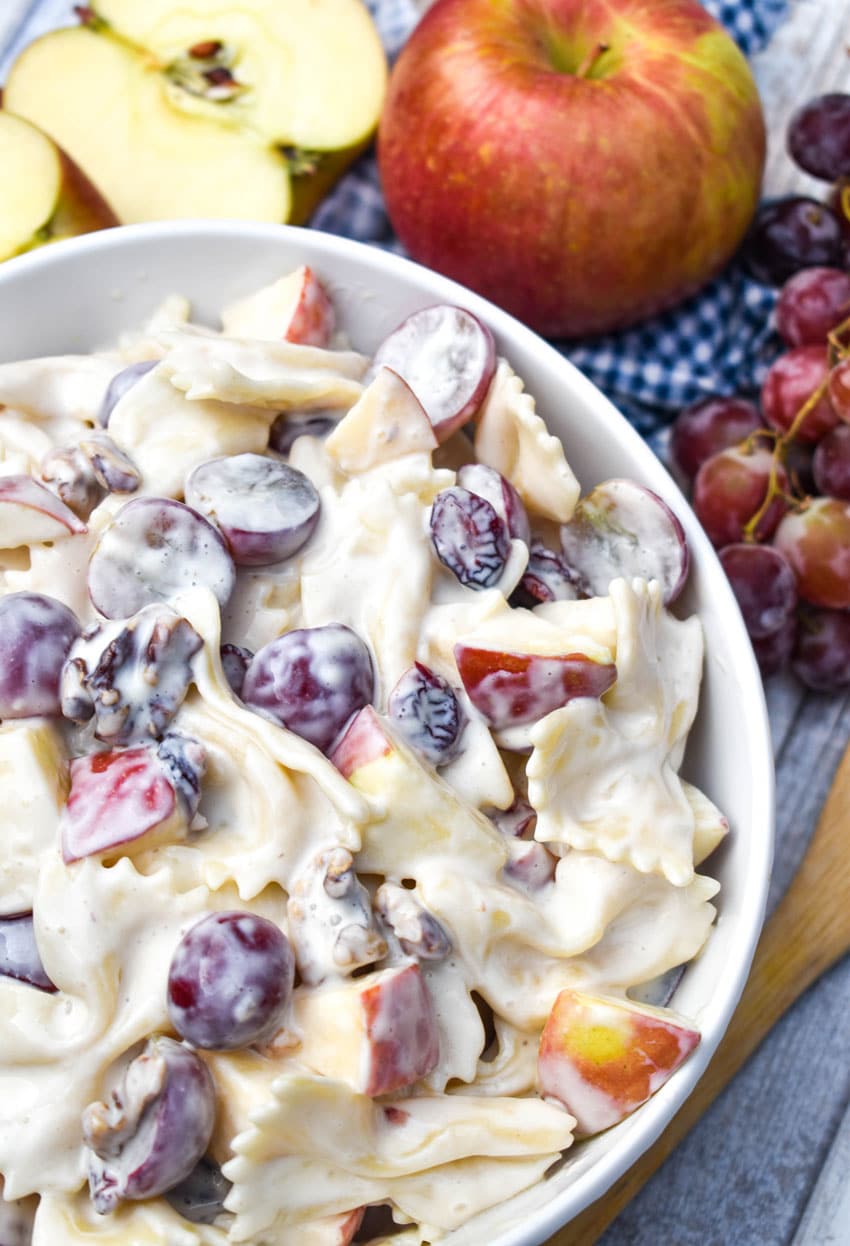 sweet pasta salad with fruit and honey in a white bowl surrounded by fresh fruits
