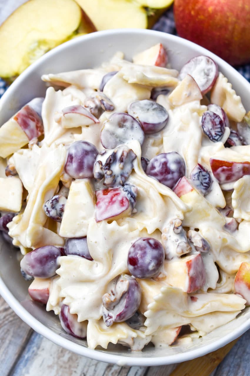 sweet pasta salad with fruit and honey in a white bowl surrounded by fresh fruits