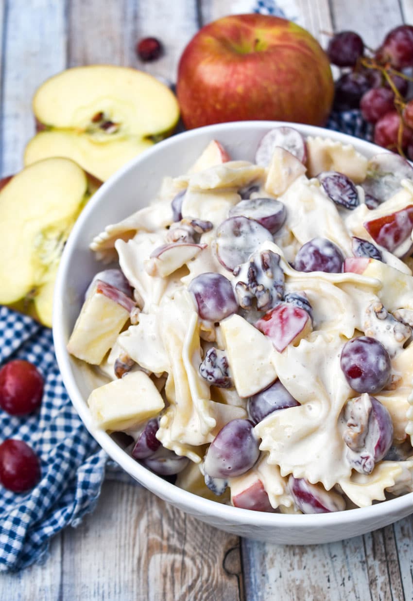 sweet pasta salad with fruit and honey in a white bowl surrounded by fresh fruits