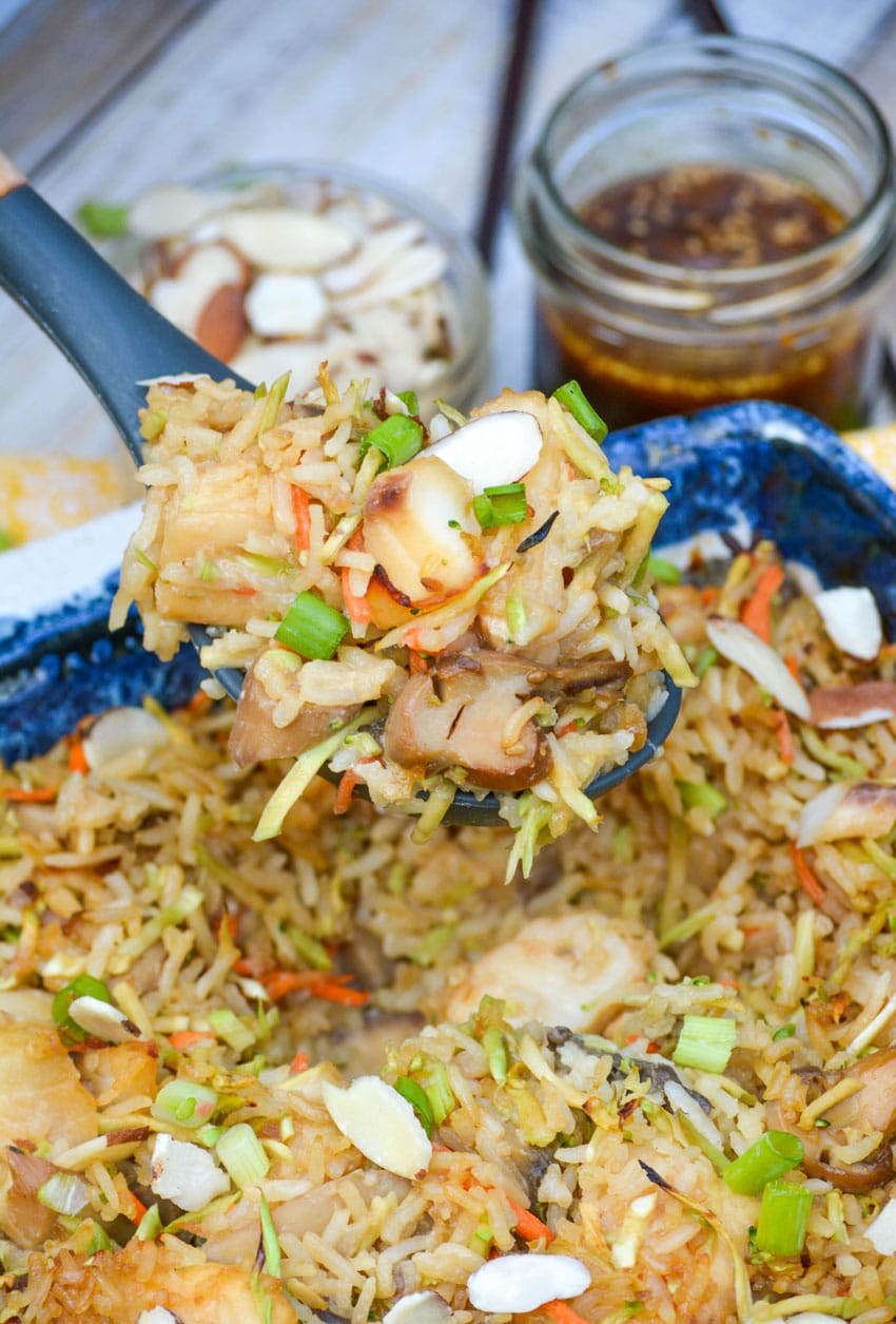 a spoon scooping teriyaki tilapia casserole out of a stone ware baking dish