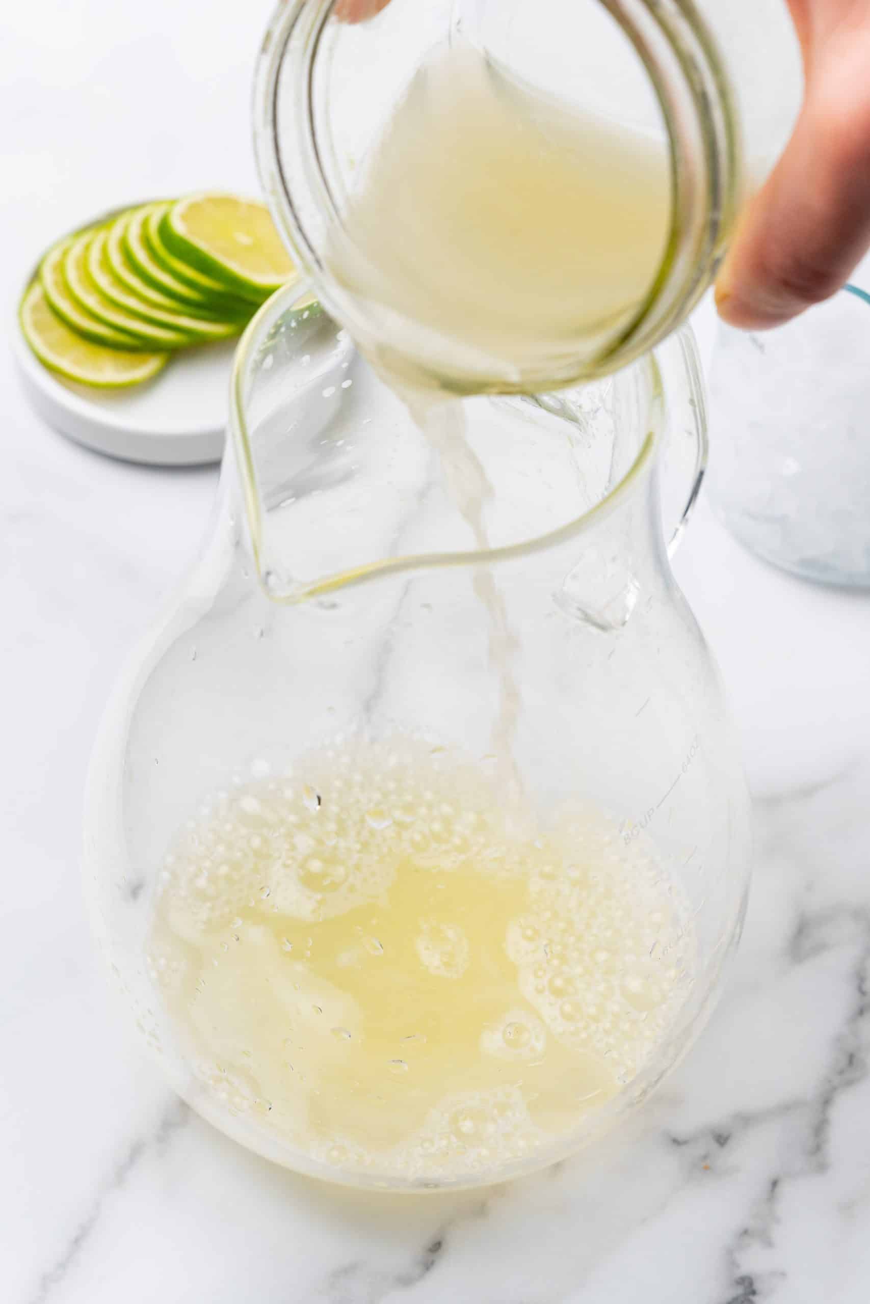 lime juice being poured into a large glass pitcher