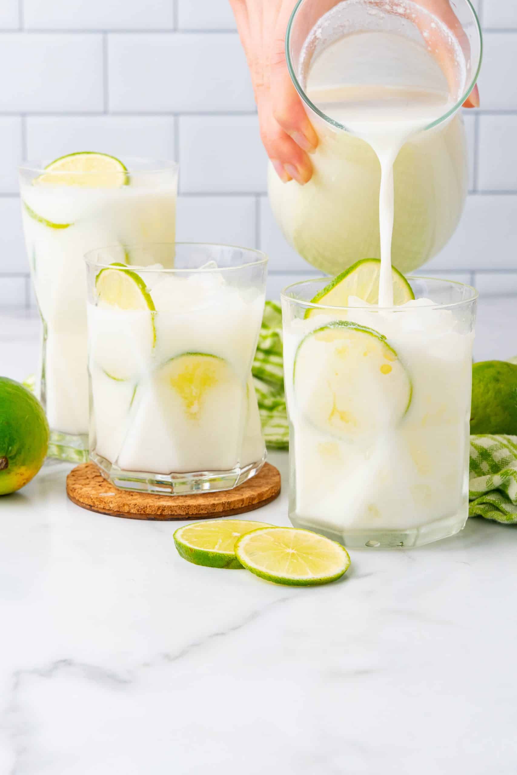 5 minute creamy limeade being poured over ice into a glass with thin slices of lime