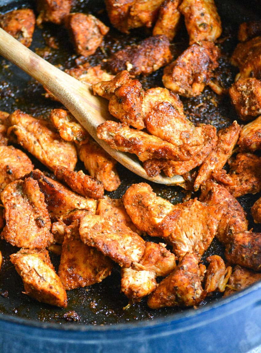 a wooden spoon scooping blackened chicken bites out of a large cast iron skillet