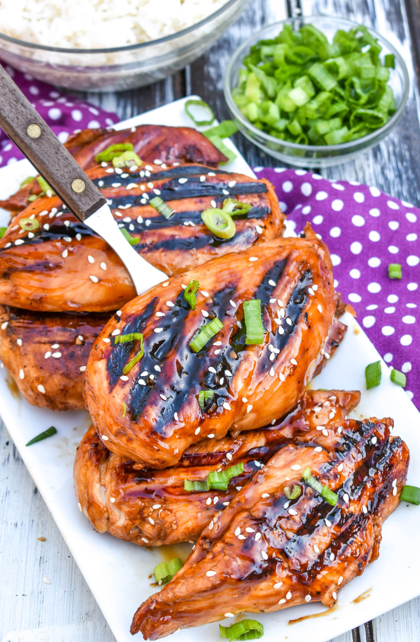 a meat fork lifting a piece of grilled huli huli chicken off a white serving plate