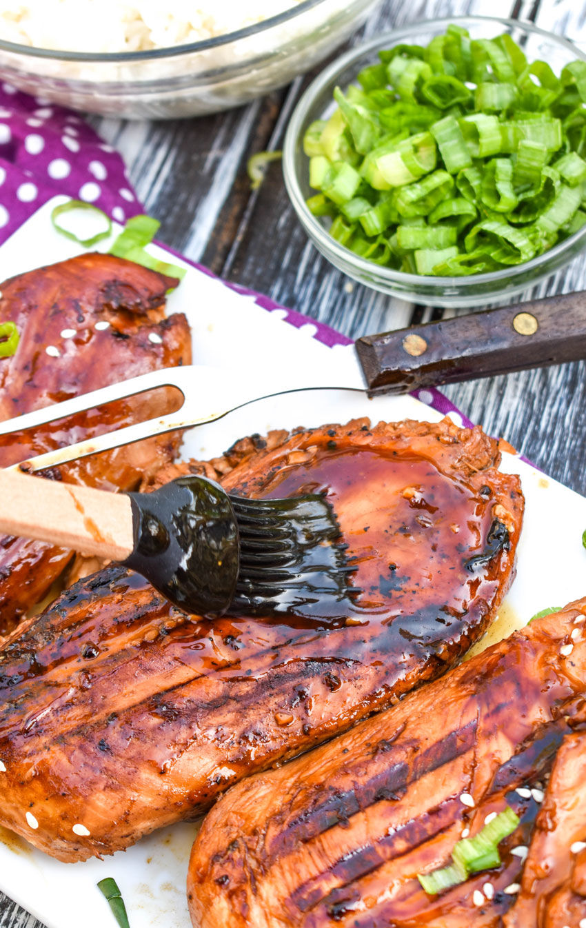 a basting brush spreading sauce on a grilled chicken breast