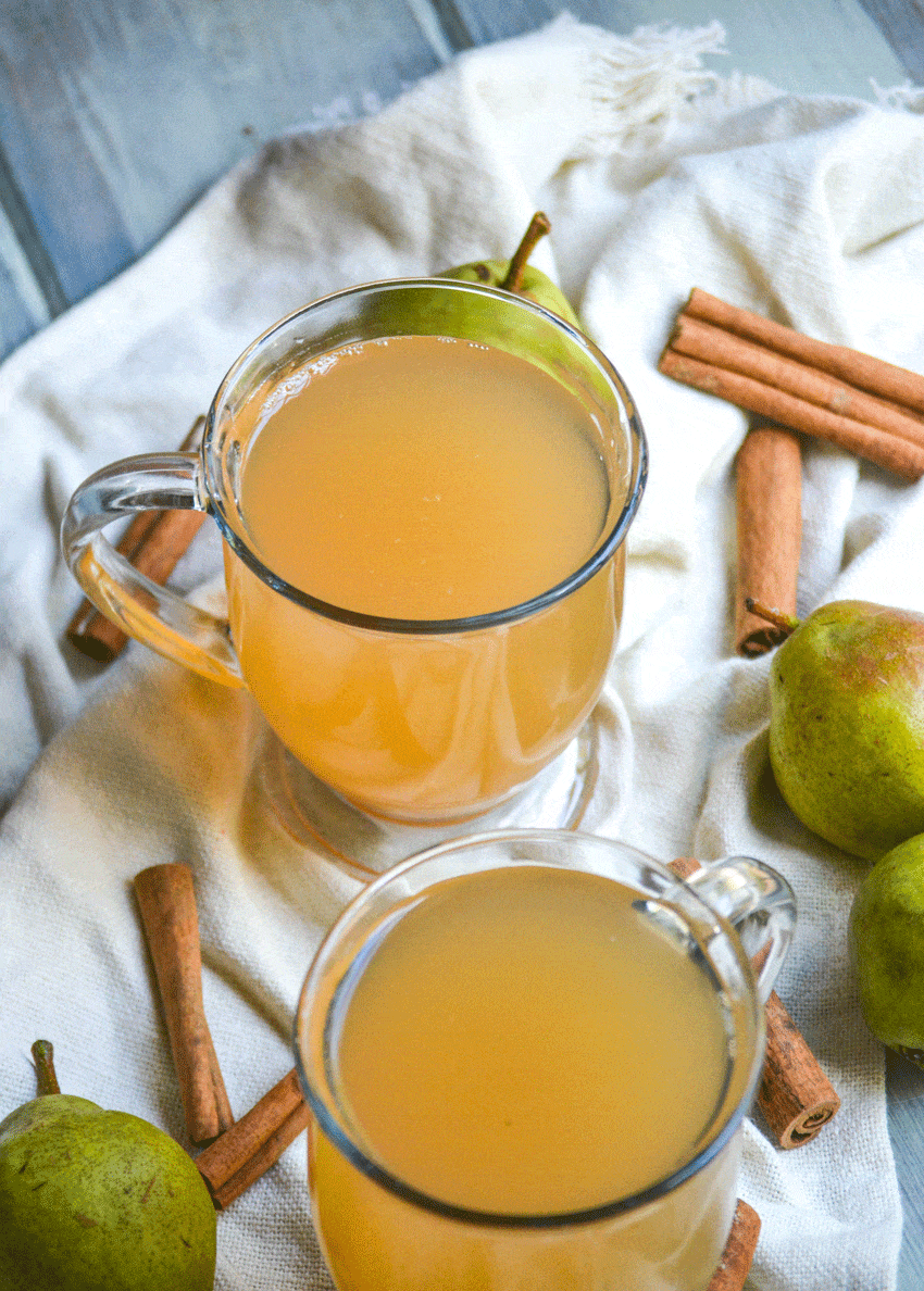 instant pot pear cider in two clear glasses surrounded by ripe pears and cinnamon sticks