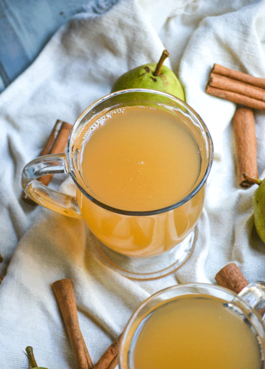 instant pot pear cider in two clear glasses surrounded by ripe pears and cinnamon sticks