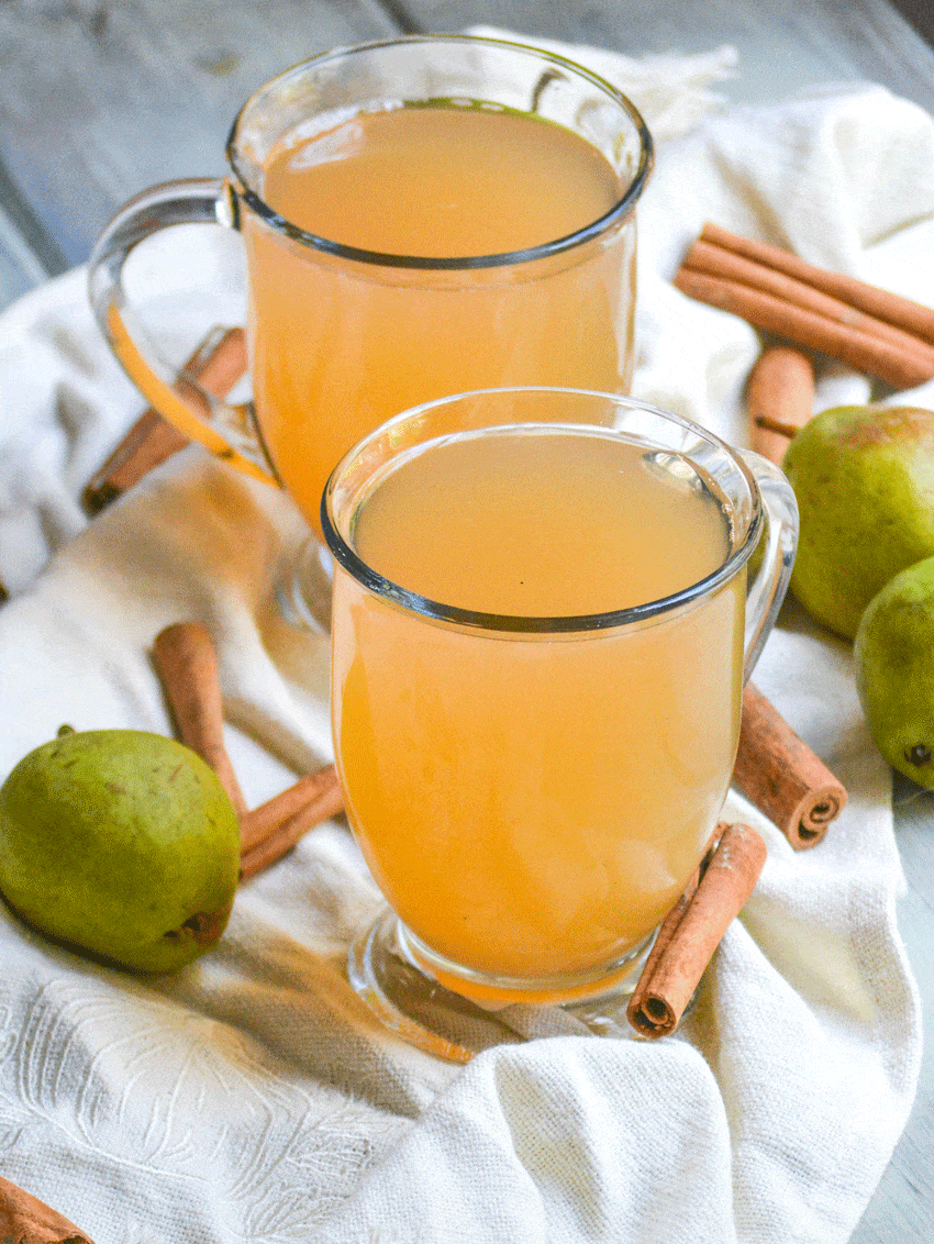 instant pot pear cider in two clear glasses surrounded by ripe pears and cinnamon sticks