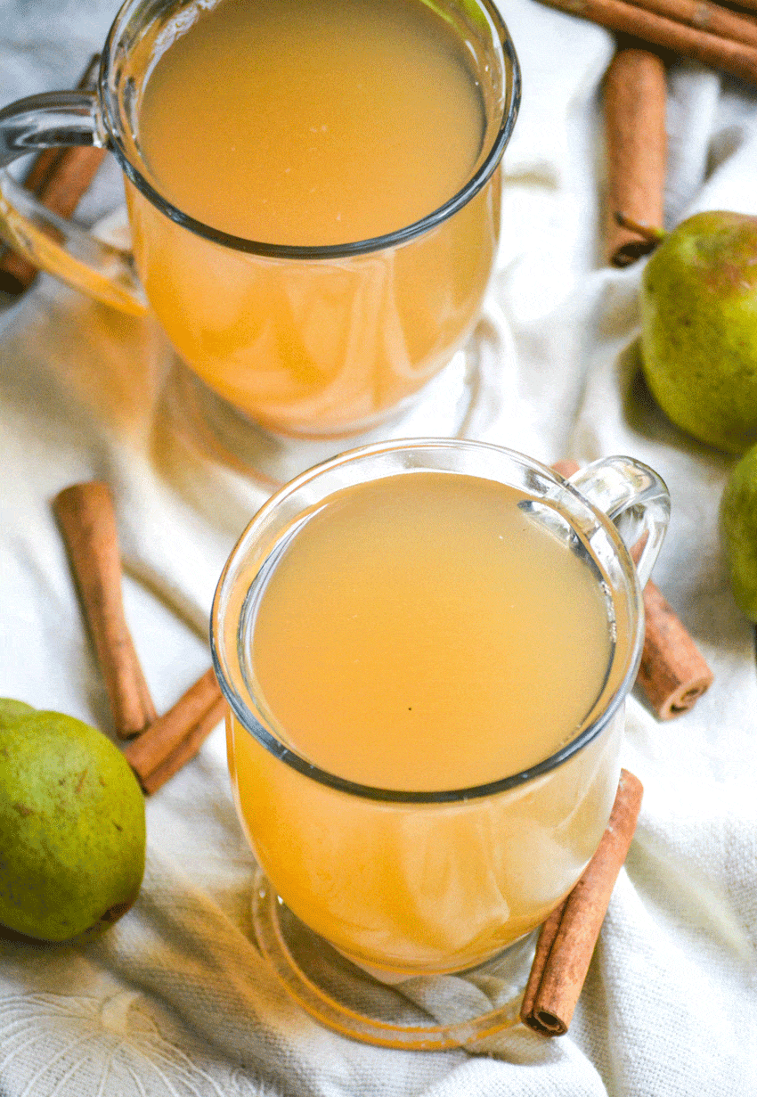 instant pot pear cider in two clear glasses surrounded by ripe pears and cinnamon sticks