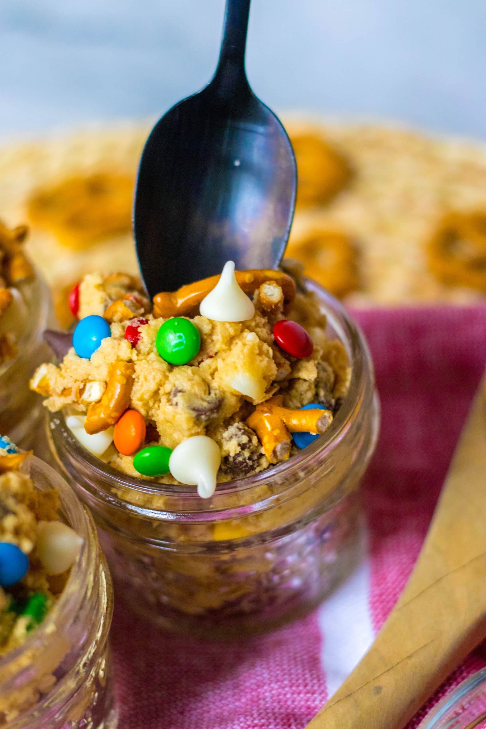 a black spoon digging into a glass jar filled with edible monster cookie dough