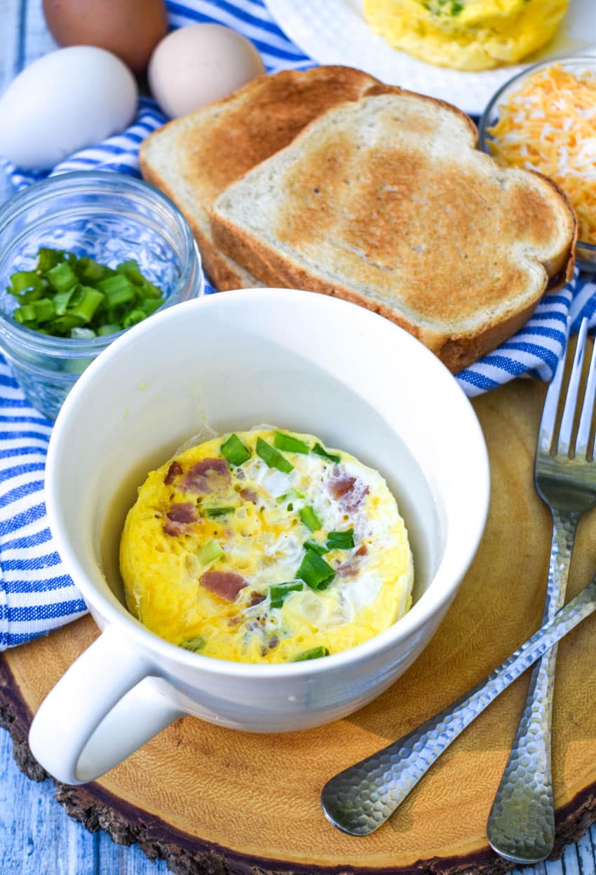 an omelet in a white mug sitting on a wooden cutting board with two silver forks on the side