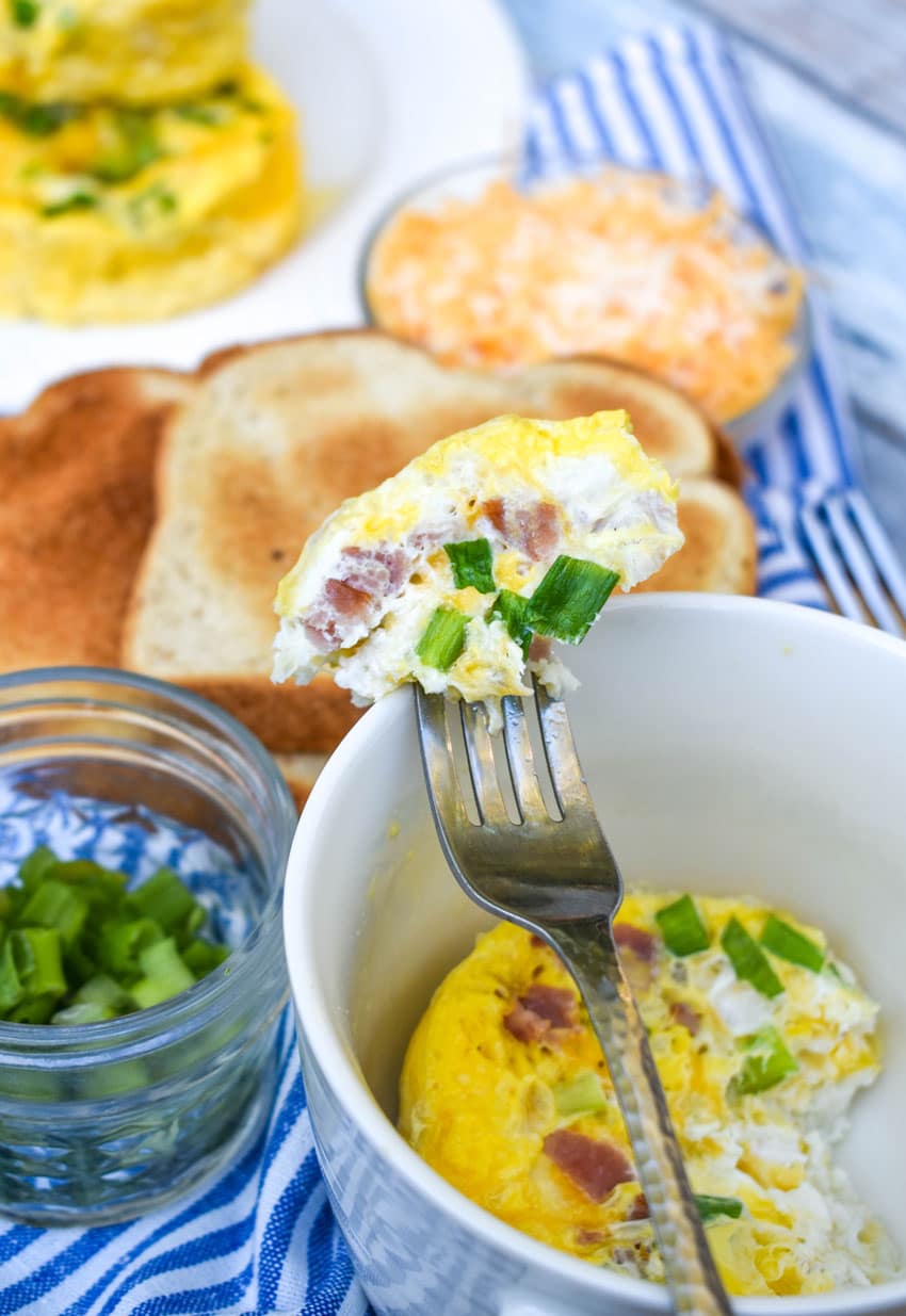 a silver fork resting on the edge of a white mug holding up a piece of mug cooked eggs