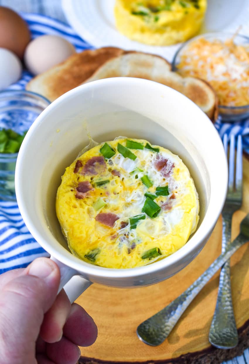 a hand holding up an omelet in a mug
