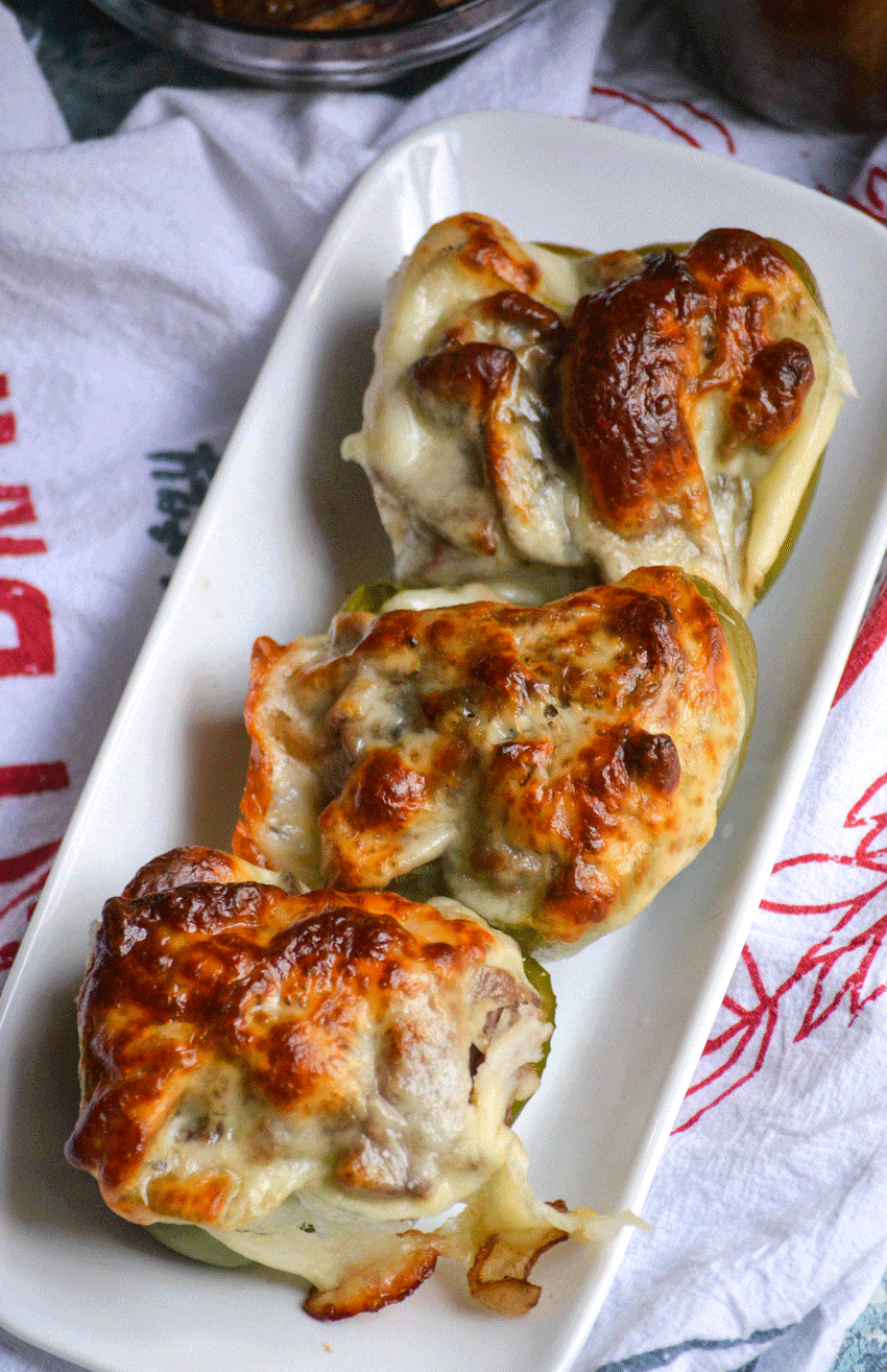 three philly cheesesteak stuffed peppers in a row on a small white platter