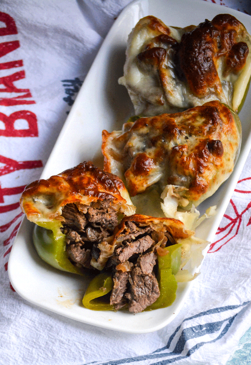 three philly cheesesteak stuffed peppers in a row on a small white platter