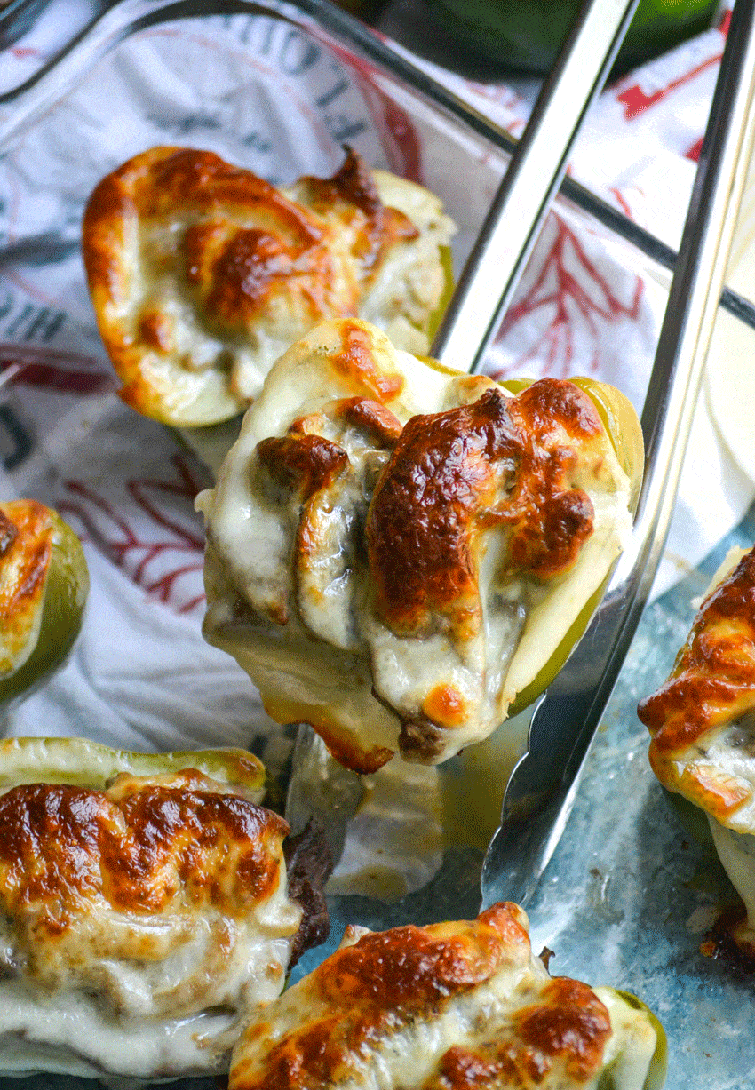 silver tongs holding up a baked cheesesteak stuffed pepper