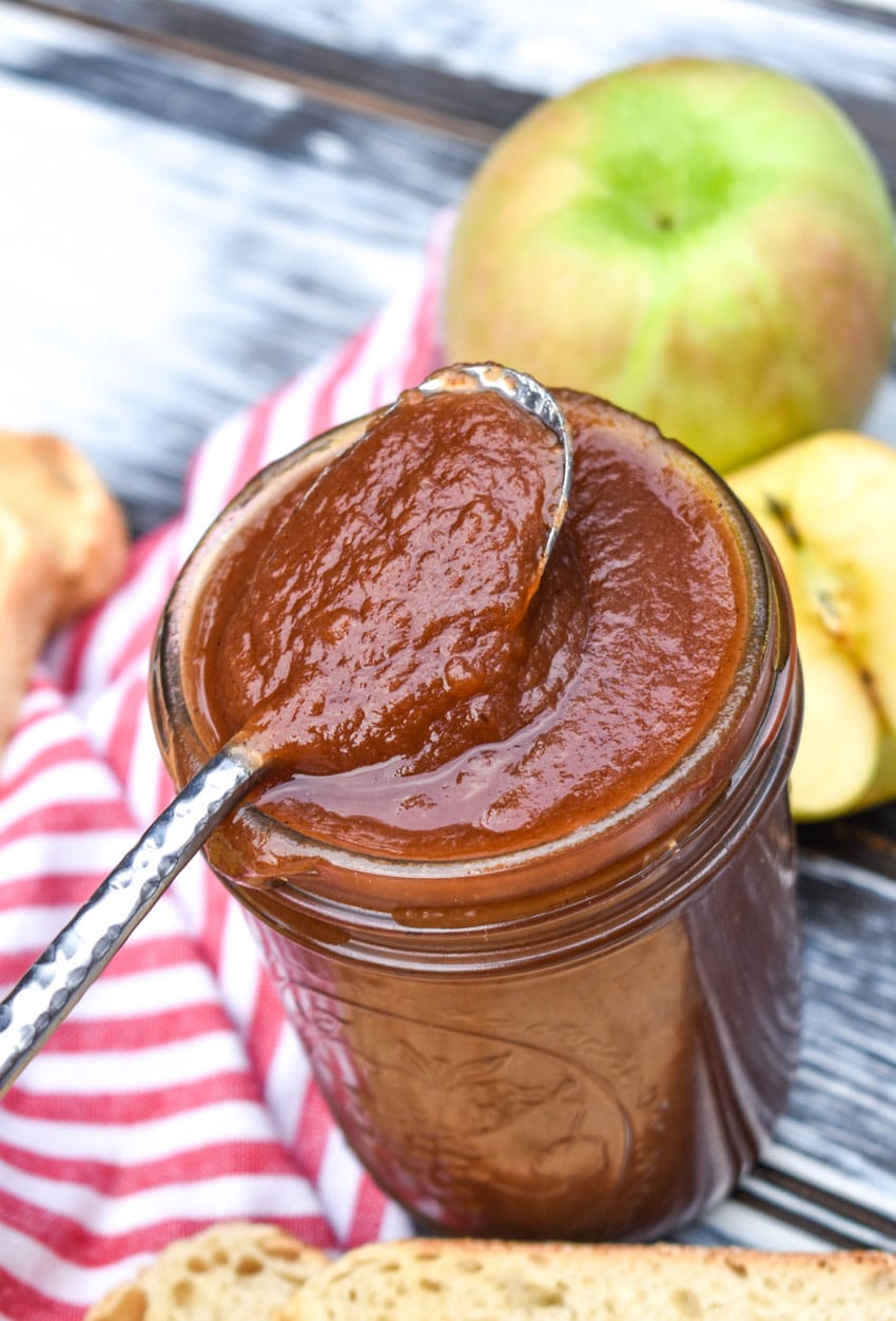 a silver spoon resting on the edge of a glass jar filled with easy crockpot apple butter