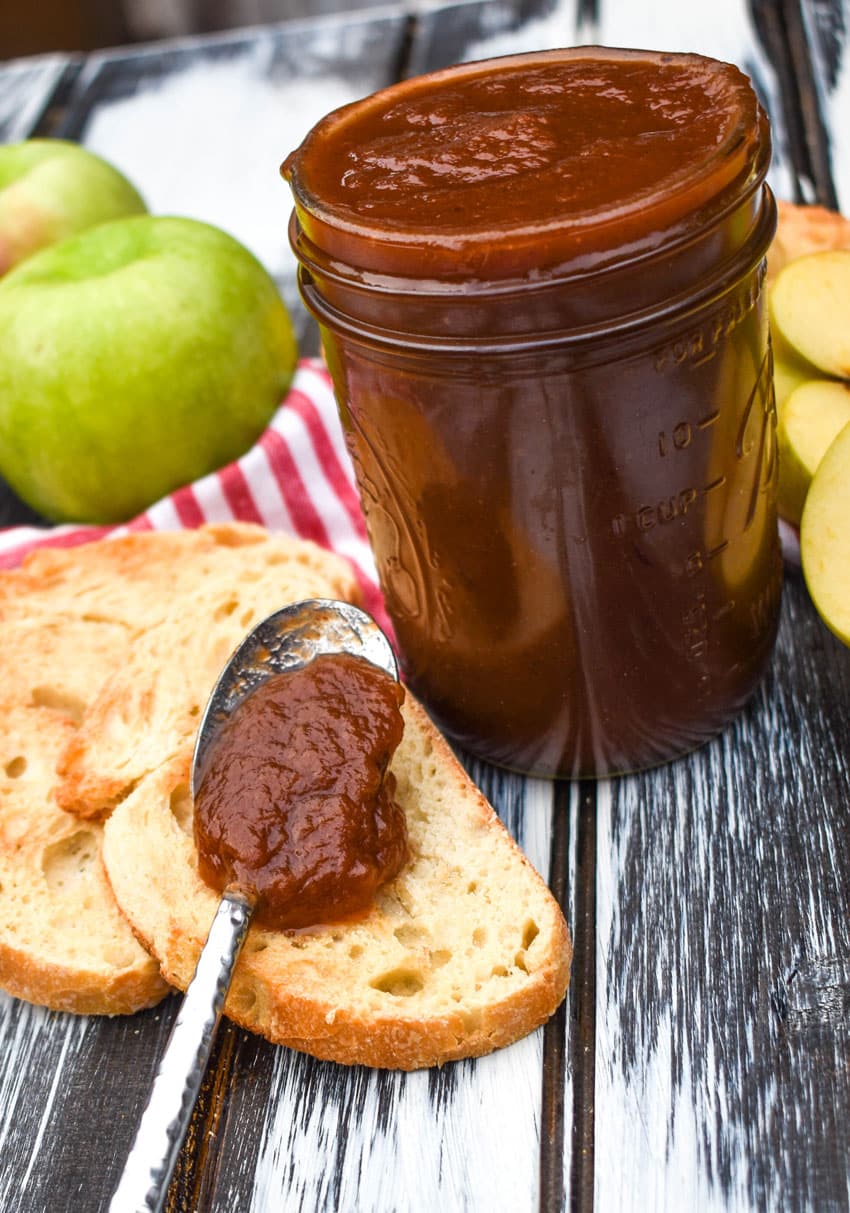 a spoon filled with crockpot apple butter resting on a slice of toasted baguette