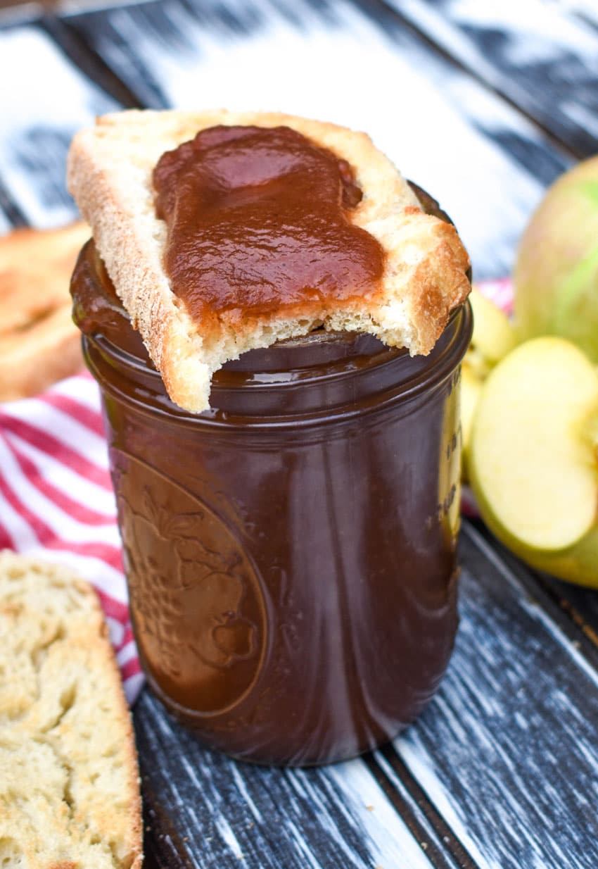 a bitten slice of toast spread with easy homemade apple butter resting on top of a glass mason jar