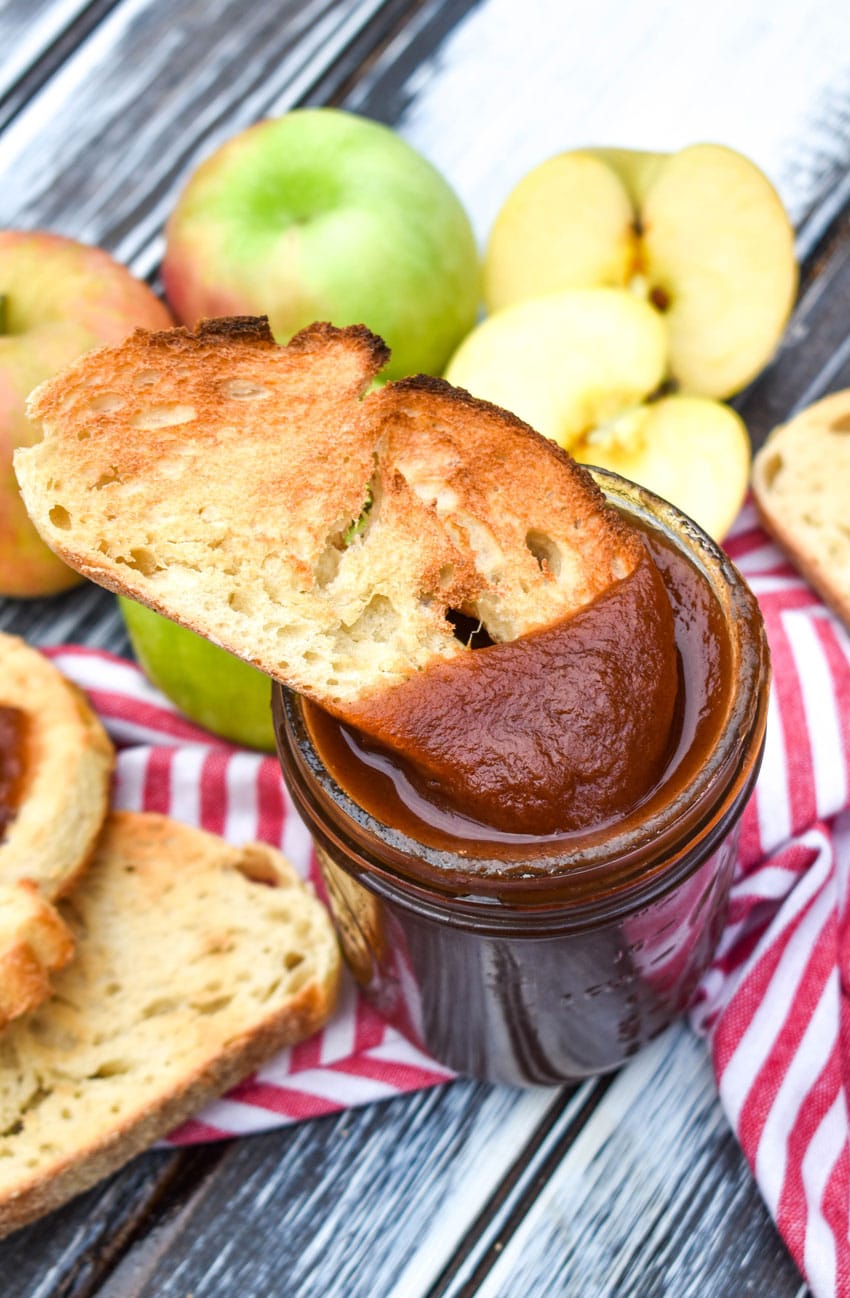a slice of toast being dipped in a glass jar filled with crockpot apple butter