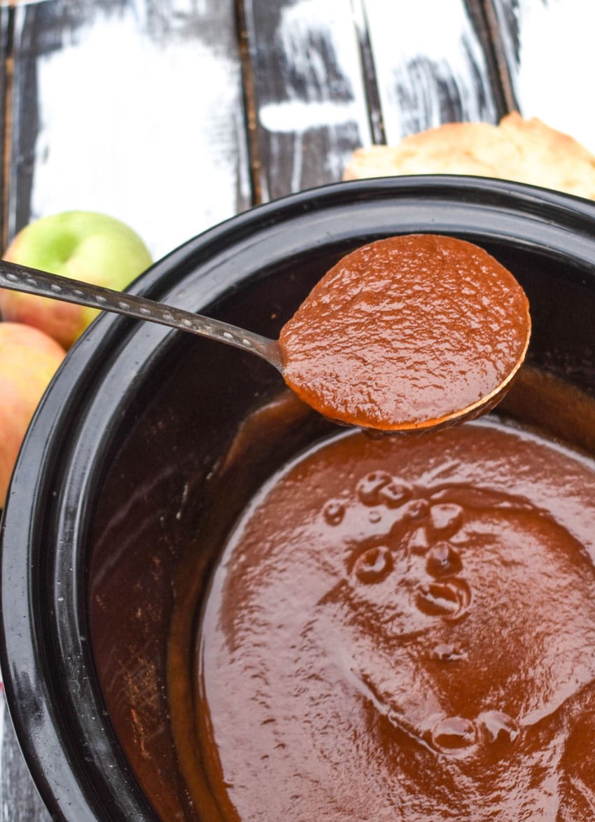 a silver ladle scooping homemade apple butter out of a black crockpot