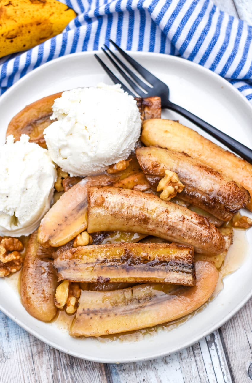 slow cooker bananas foster on a white plate topped with scoops of vanilla ice cream