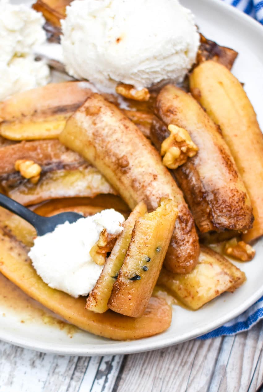 a black fork scooping slow cooker bananas foster and vanilla ice cream off of a white plate
