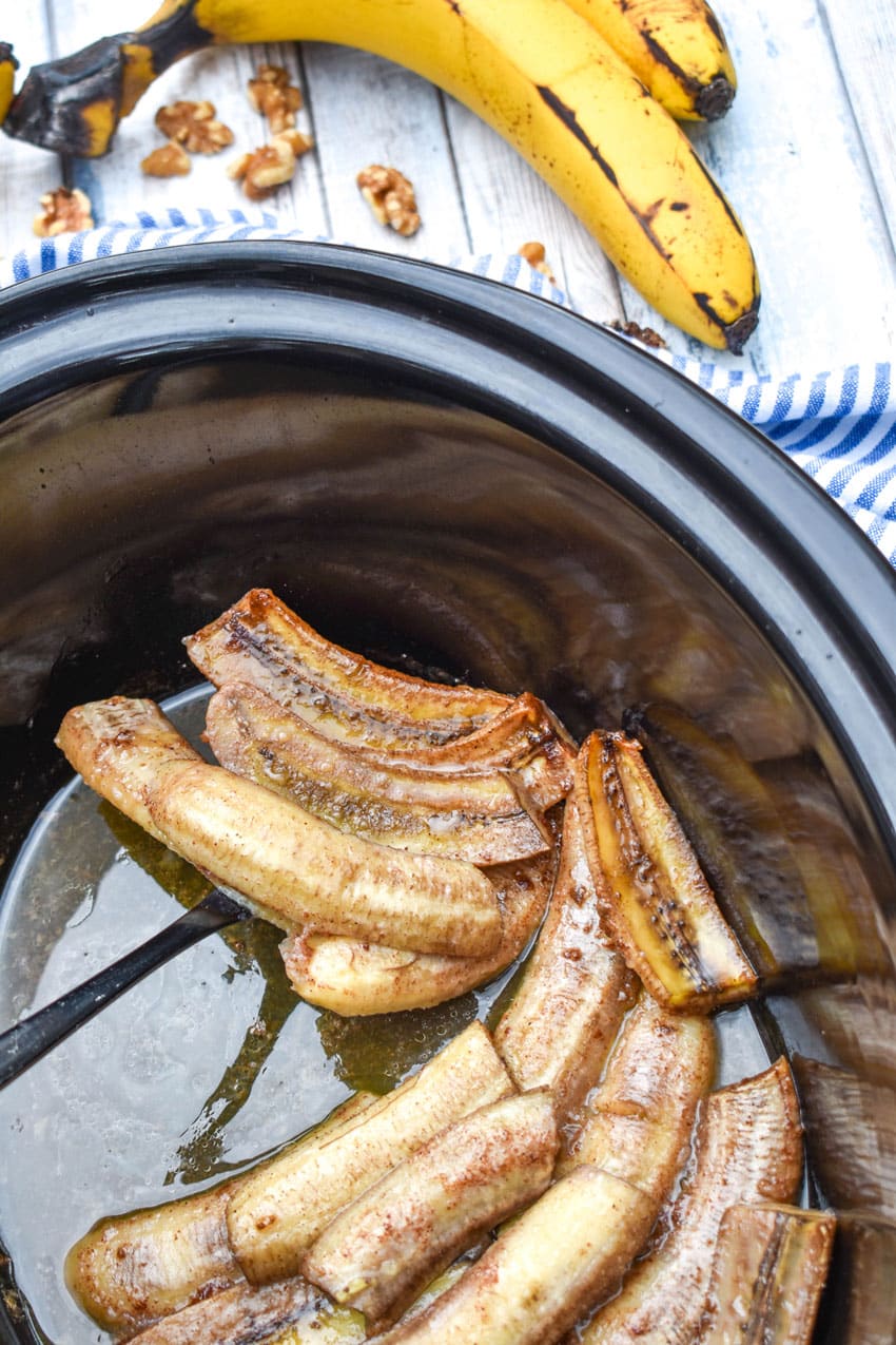 a black serving spoon scooping slow cookers bananas foster out of a black crockpot