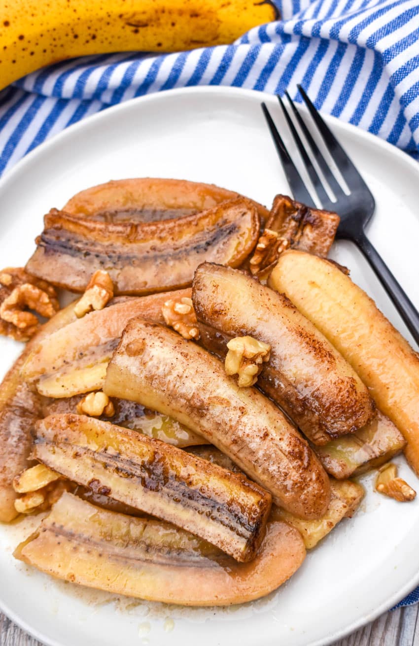 slow cooker bananas foster on a white plate topped with chopped walnuts with a black fork on the side