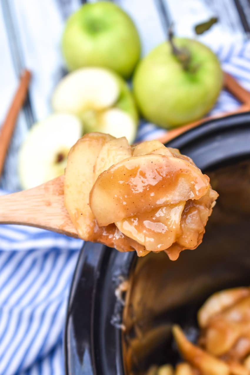 a wooden spoon holding up a scoop of crock pot fried apples