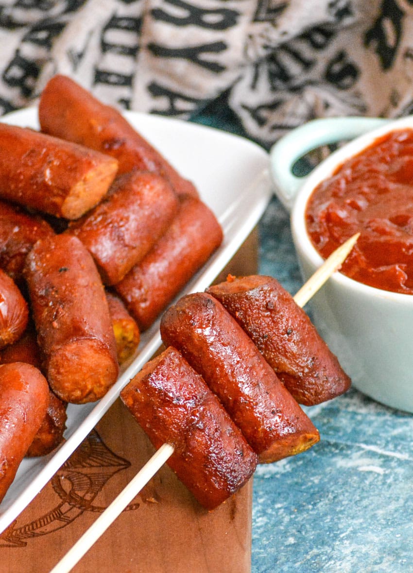 smoked hot dog burnt ends threaded on a wooden skewer resting on a wooden cutting board