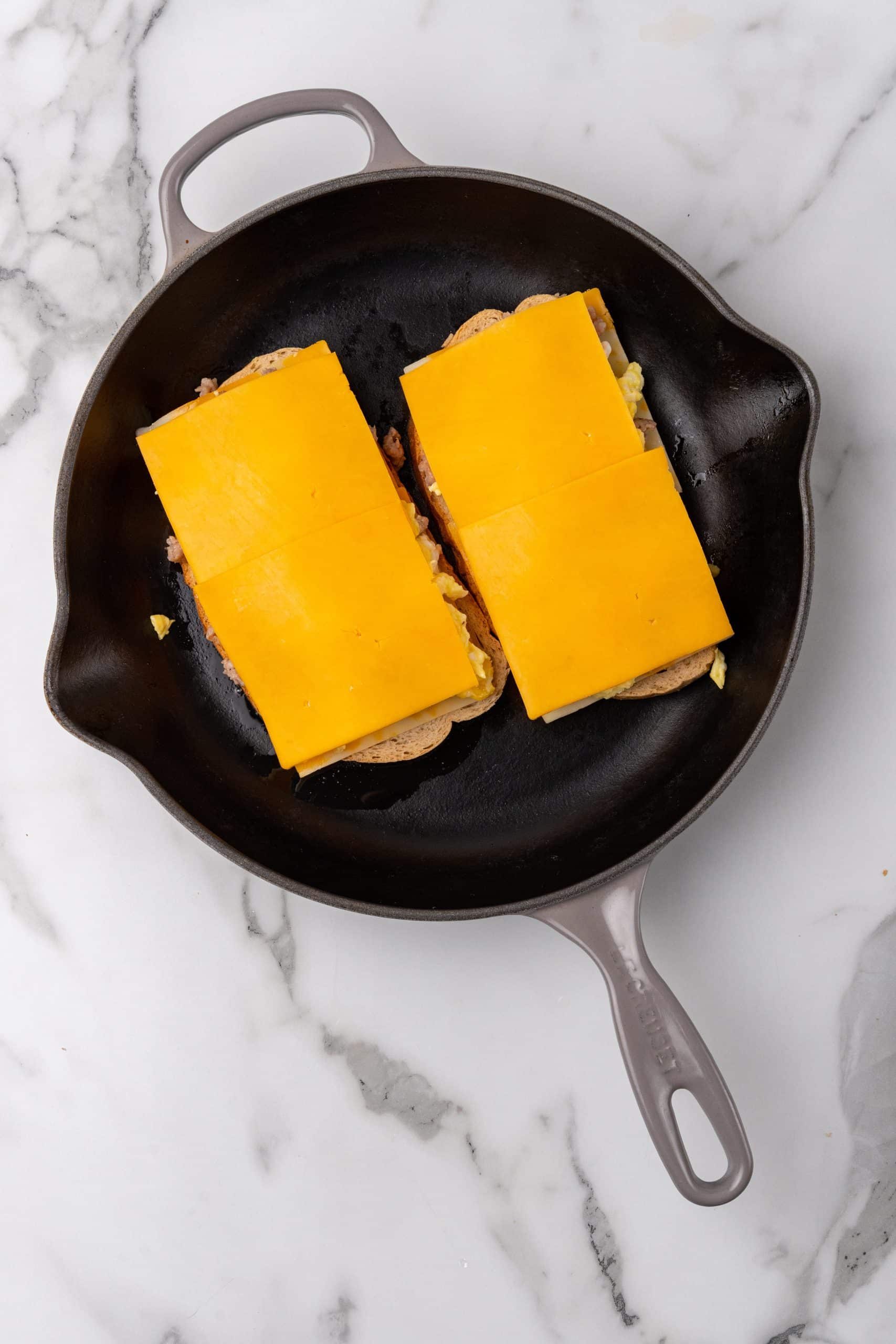 two cheese topped breakfast sandwiches in a black skillet