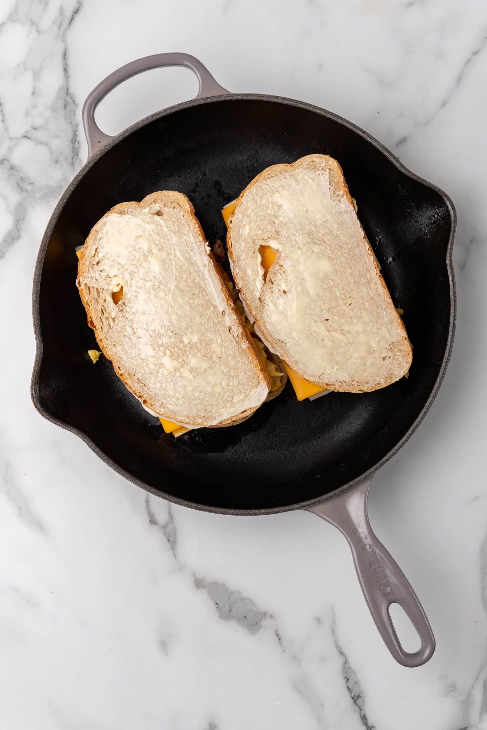 two buttered grilled cheese with sourdough bread in a black skillet