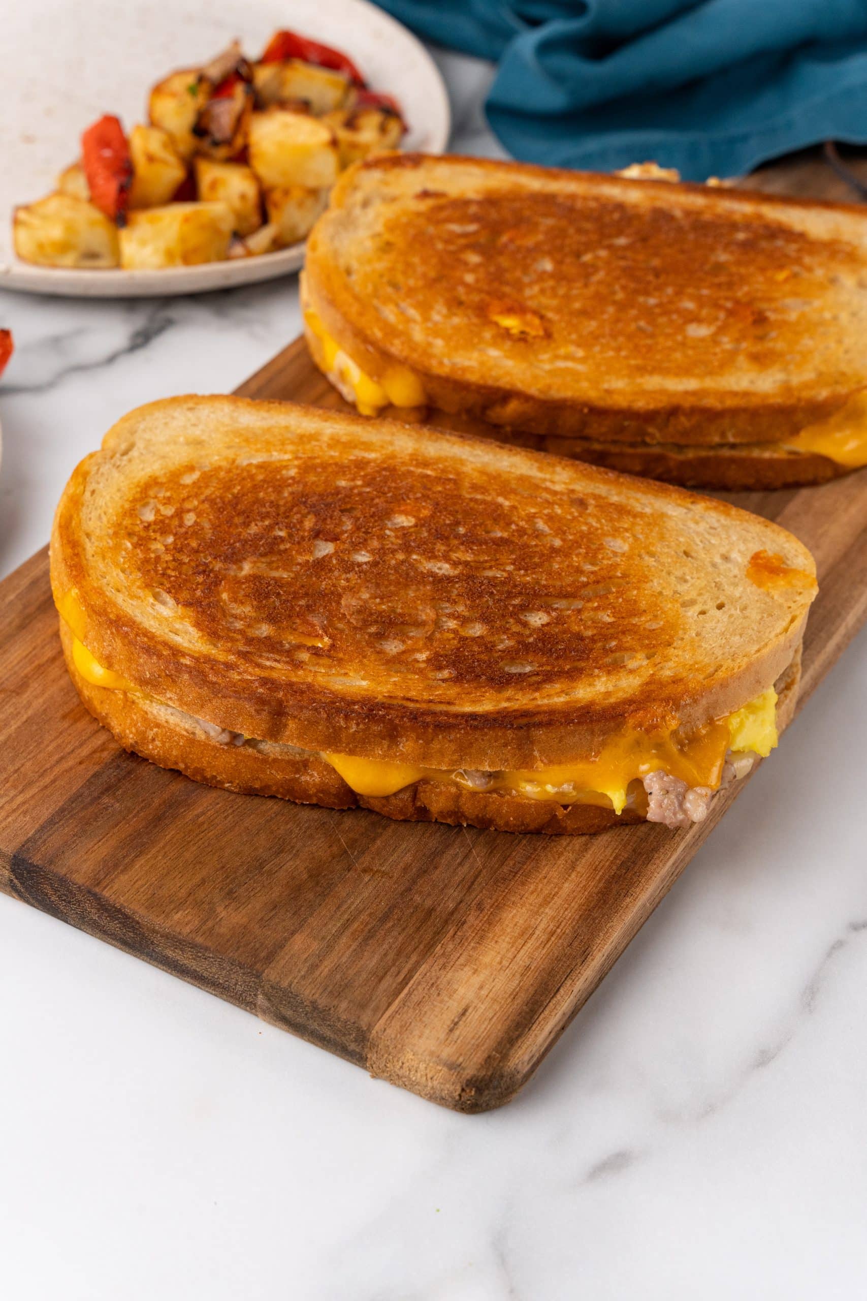 two crispy grilled cheese and egg sandwiches on a wooden cutting board