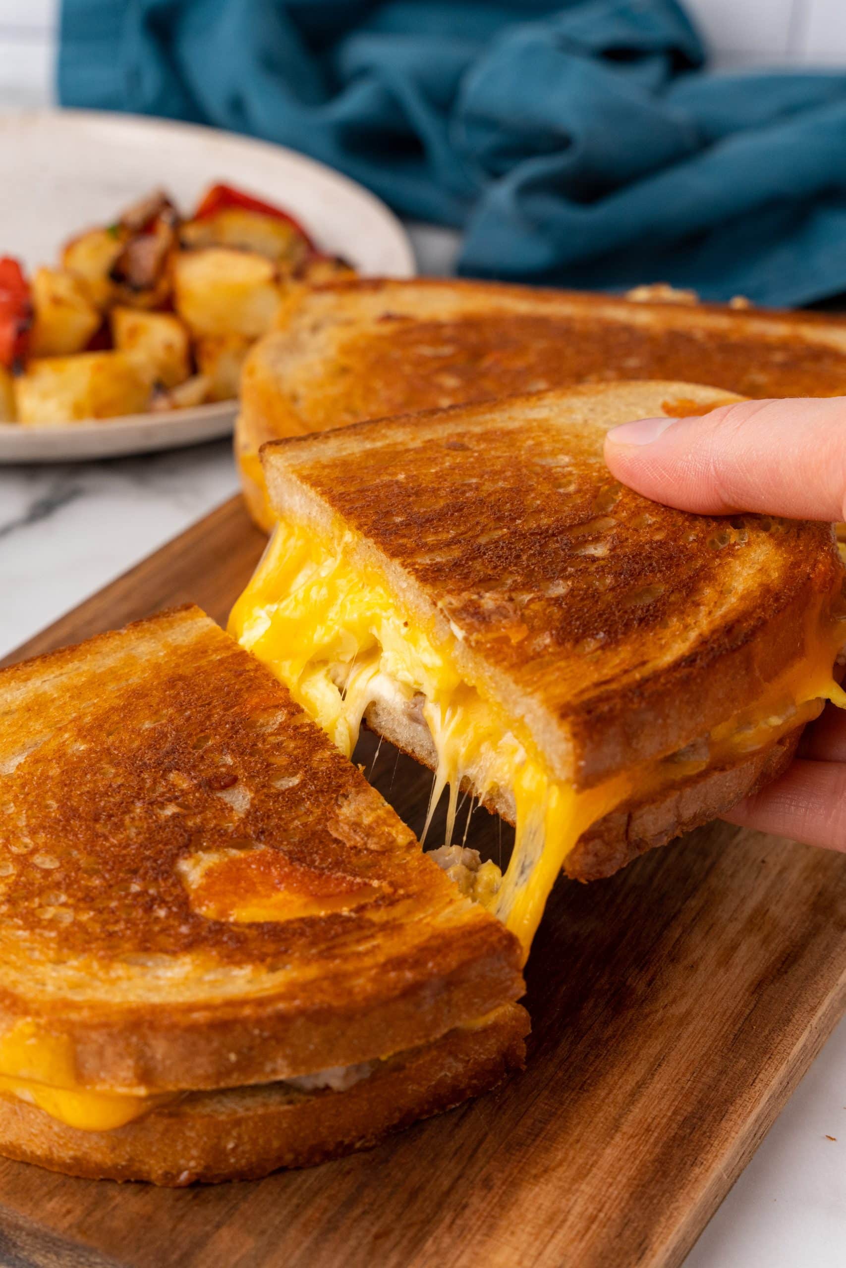two halves of a crispy grilled breakfast sandwich with cheese being pulled apart on a wooden cutting board