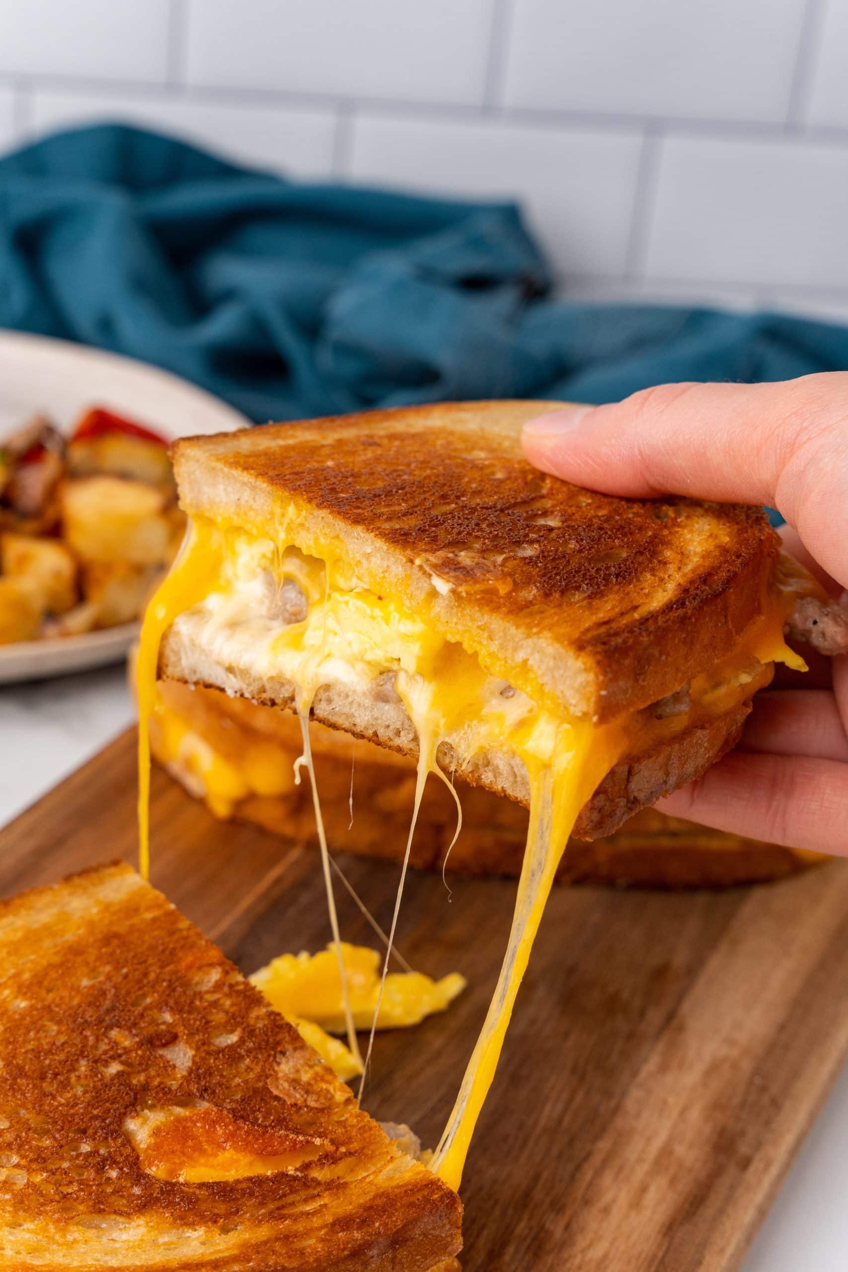 two halves of a crispy grilled breakfast sandwich with cheese being pulled apart on a wooden cutting board