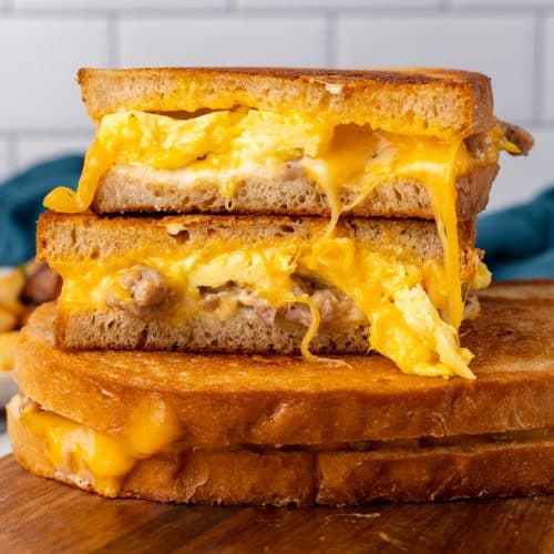two halves of the best breakfast grilled cheese stacked on top of another sandwich resting on a wooden cutting board