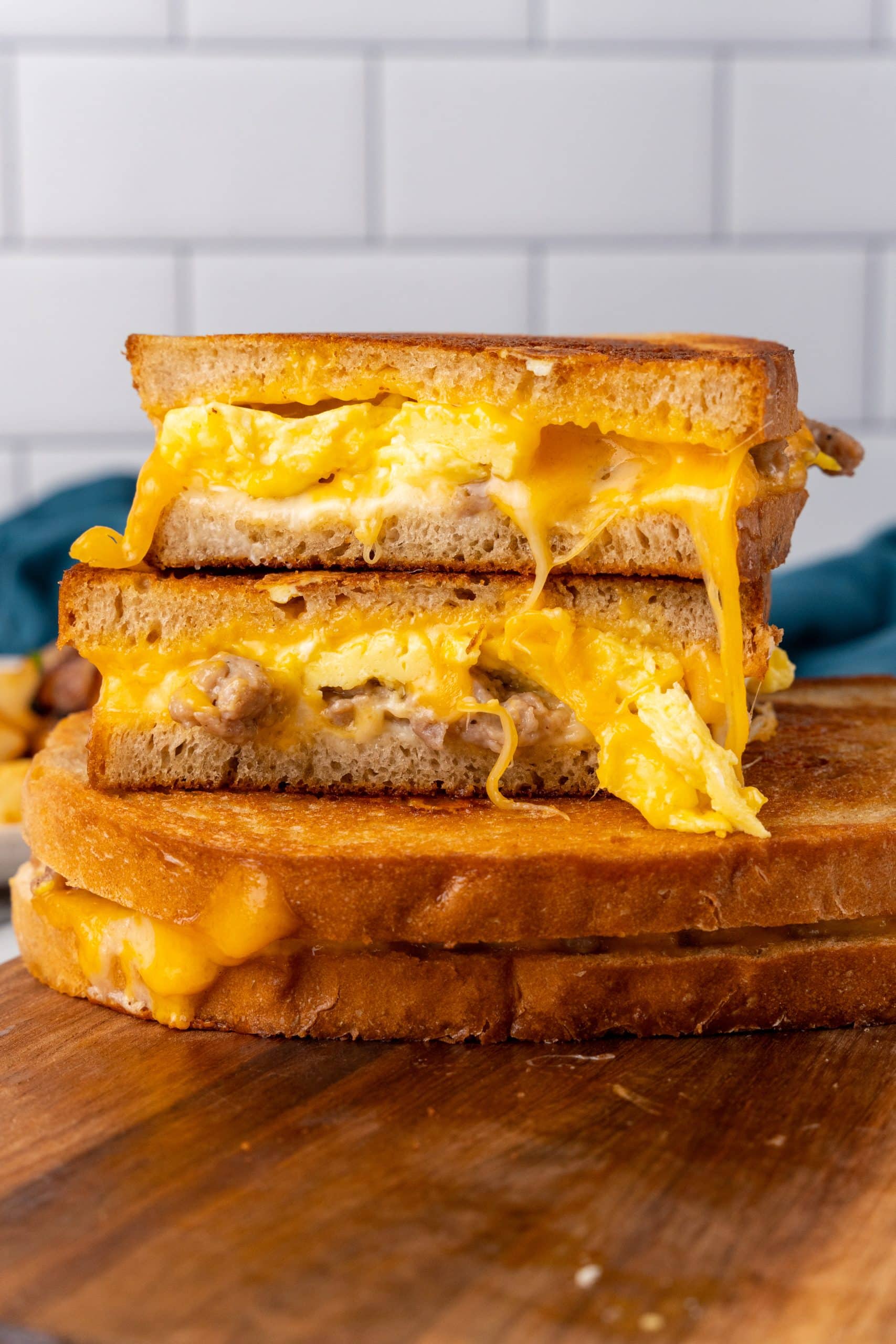 Breakfast Grilled Cheese Sandwich two halves of the best breakfast grilled cheese stacked on top of another sandwich resting on a wooden cutting board