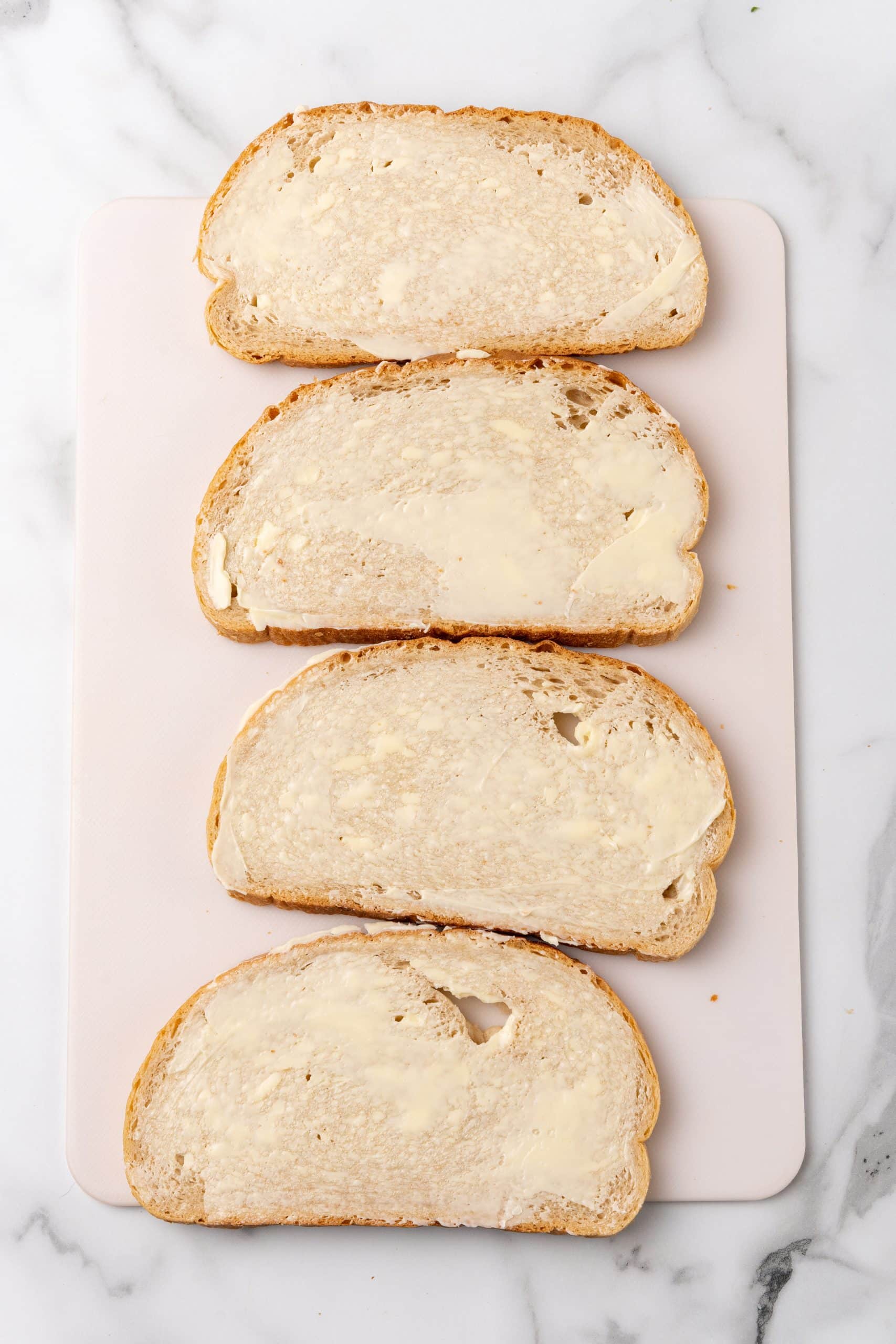four buttered slices of bread on a white cutting board