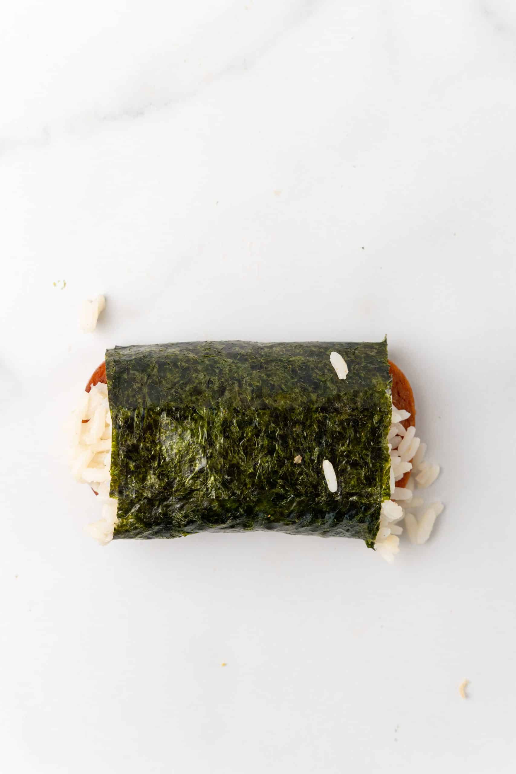 a piece of wrapped spam misubi on a marble countertop