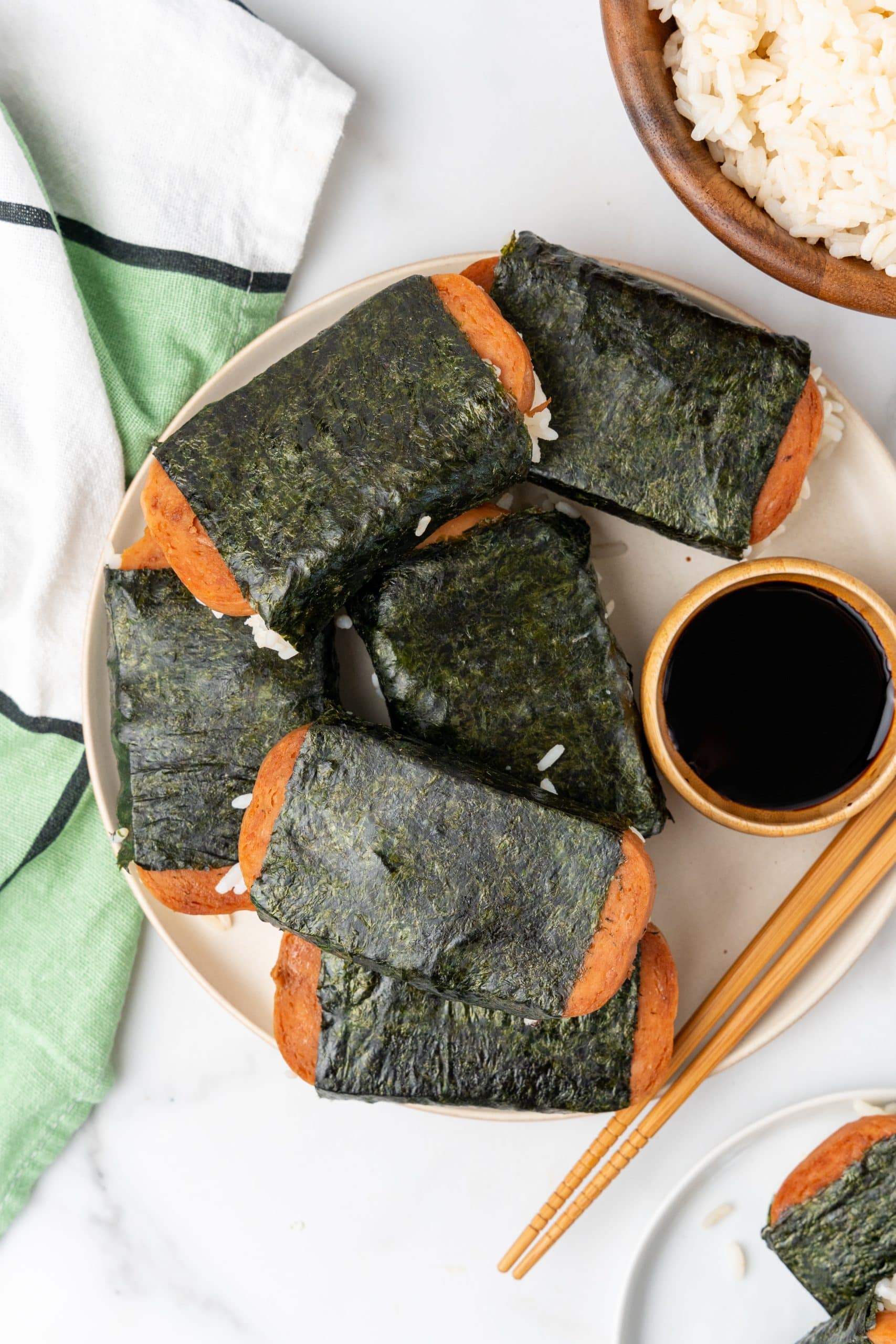pieces of spam misubi on a white plate with a small wooden bowl filled with soy sauce on the side