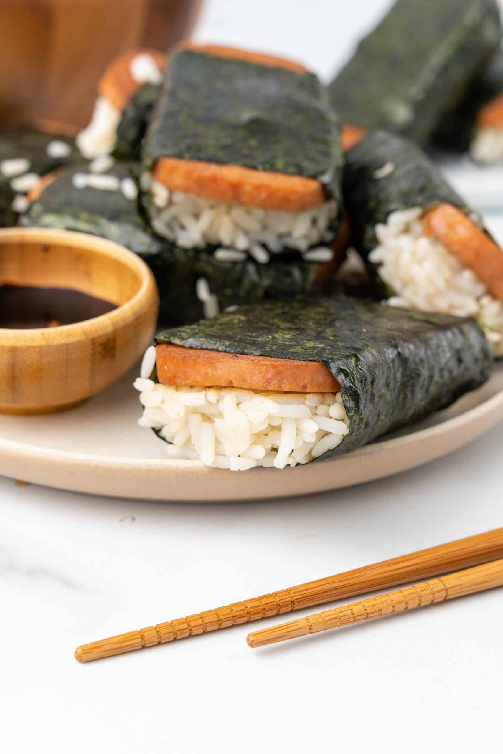 pieces of spam misubi on a white plate with small bowl of dark dipping sauce on the side