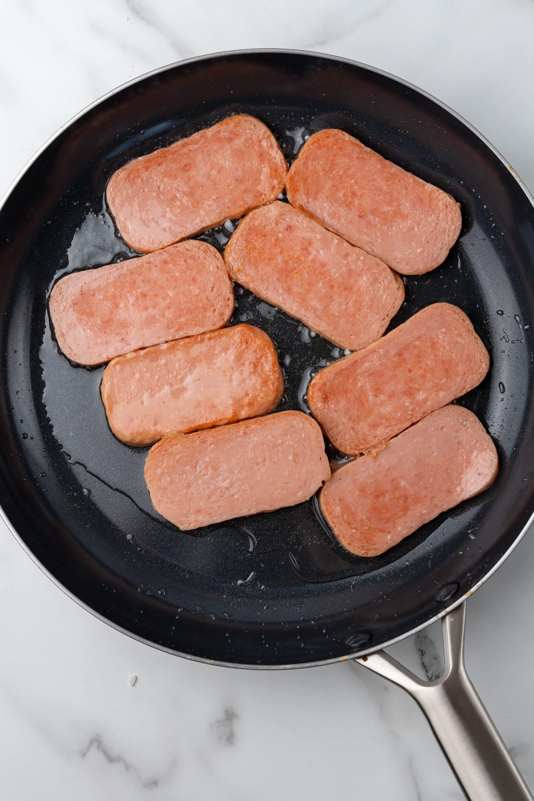 slices of spam cooking in hot oil in a black skillet