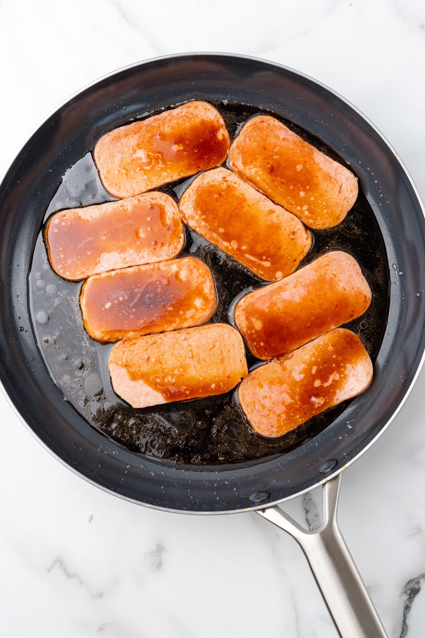sauced slices of spam in a large black skillet