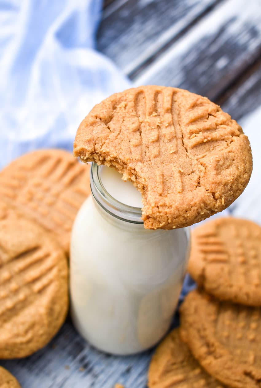 a bitten peanut butter cookie resting on a glass jar of milk
