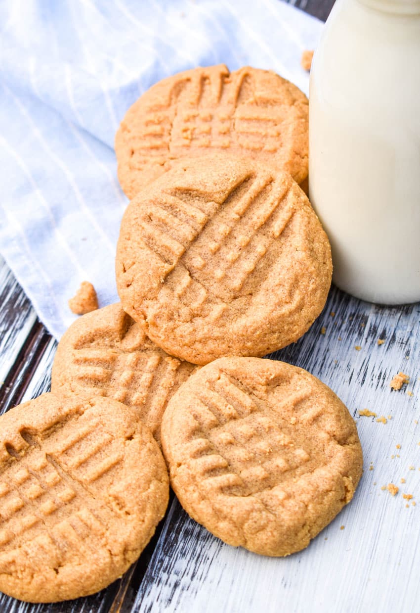 three ingredient peanut butter cookies stacked around a glass jar of milk