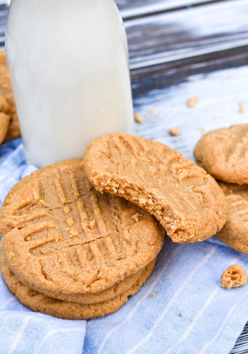three ingredient peanut butter cookies stacked around a glass jar of milk