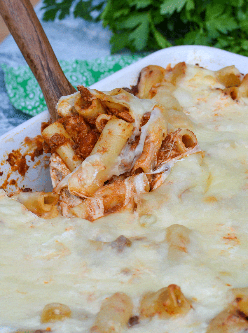 a wooden spoon scooping cheesy baked ziti out of a casserole dish