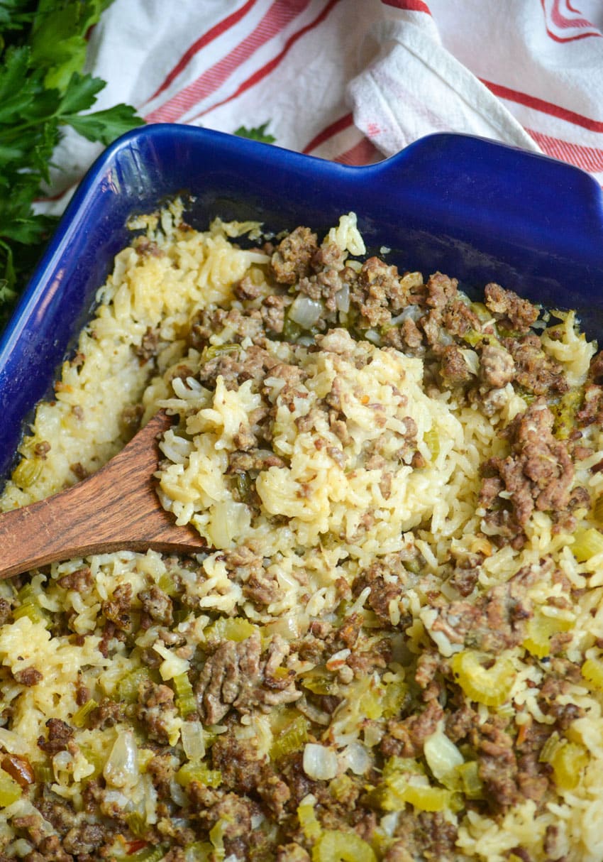 a wooden spoon stuck in ground beef and rice casserole in a blue baking dish